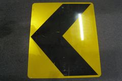 Sign-Chevron/arrow, large >, black on yellow metal, 30"w x 36"t, stock number S-1912