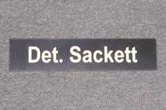 Sign-Det. Sackett, plastic, black, 11"w x 2 ½"t, stock number S-2044b